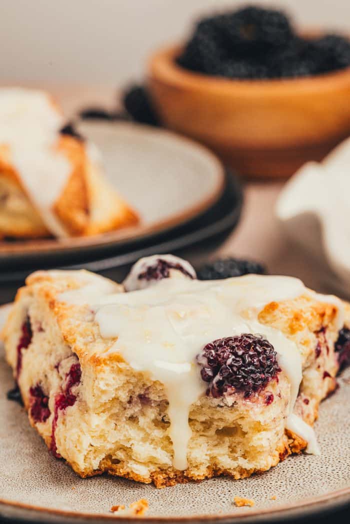 A plate with a glazed blackberry scone on it with a bite taken out of it.