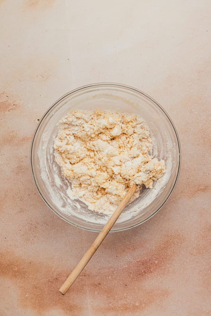 A glass bowl with scone dough in it and a spatula.