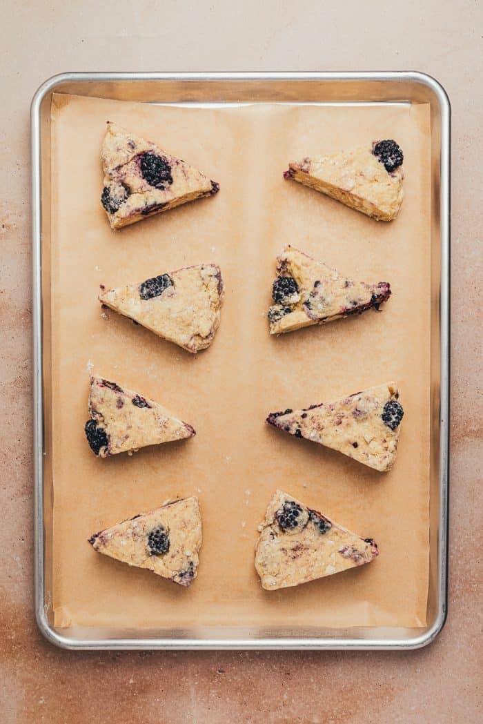 The scone dough cut into wedges on a baking sheet with parchment paper.