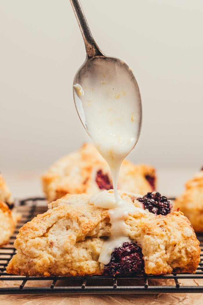 A blackberry scone with glaze dripping on it.