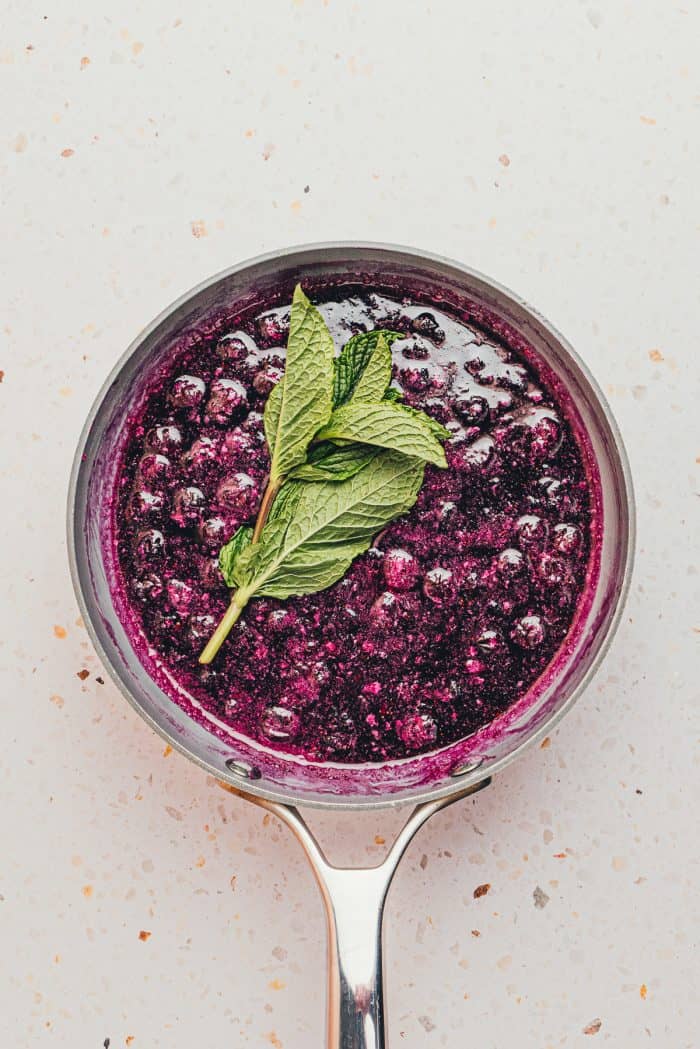 A saucepan with cooked blueberry syrup and fresh mint.
