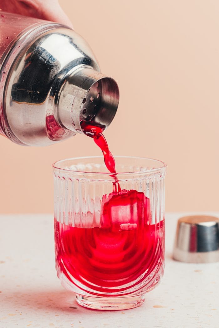 A cocktail shaker pouring the drink into a glass.