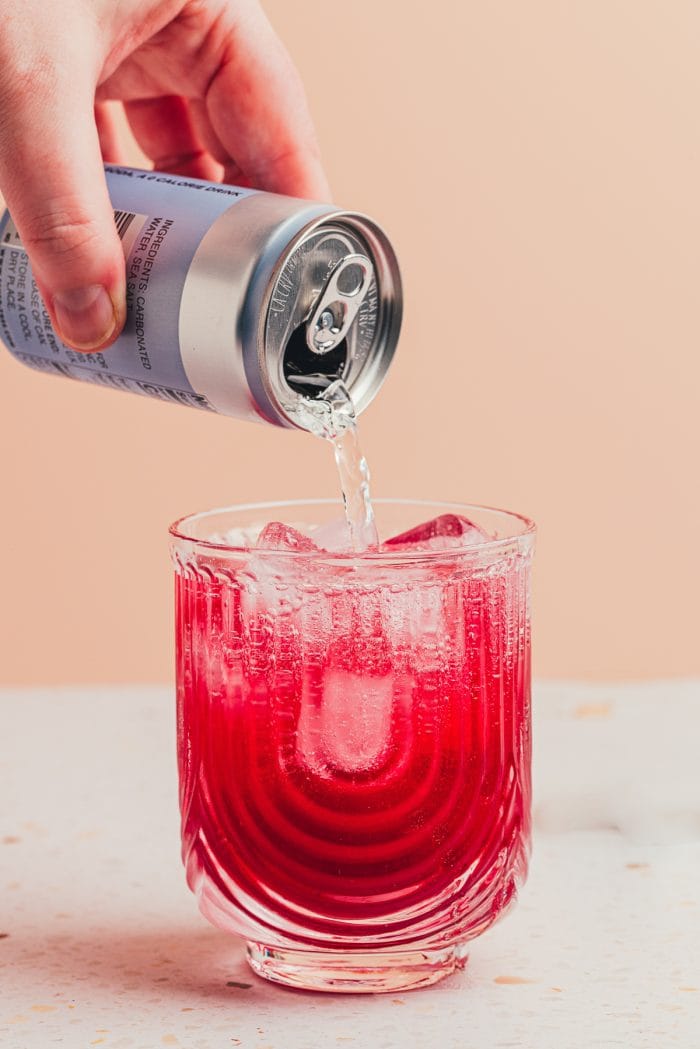 A blueberry cocktail being topped with club soda.