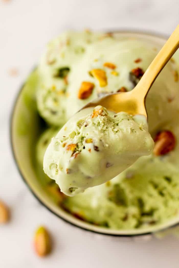 A bowl with many scoops of no churn Pistachio Ice cream and a spoon holding a spoonful of ice cream.
