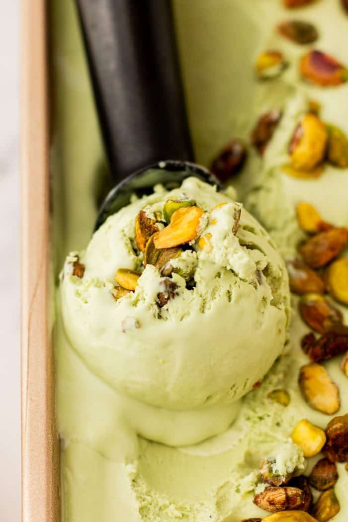 A loaf pan with homemade pistachio ice cream and an ice cream scoop, scooping some ice cream.