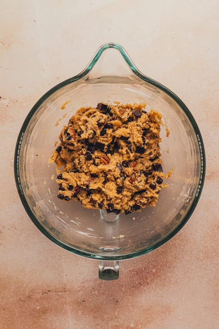 Chocolate chips mixed into the cookie dough in a glass mixing bowl.