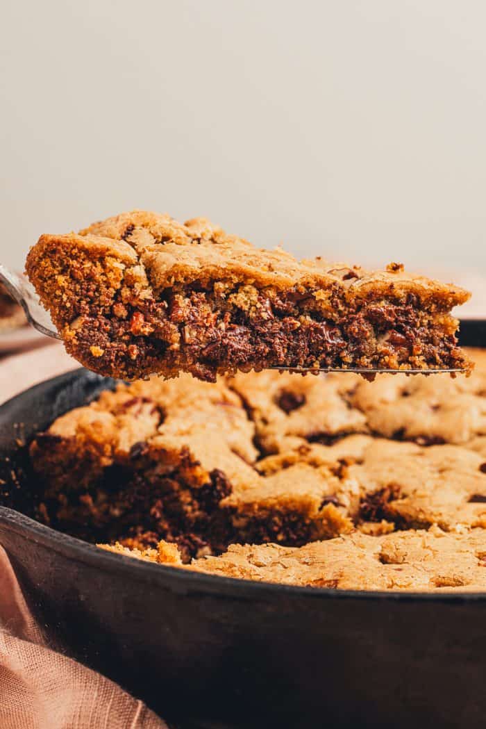 A slice of chocolate chip cookie being removed from the skillet.