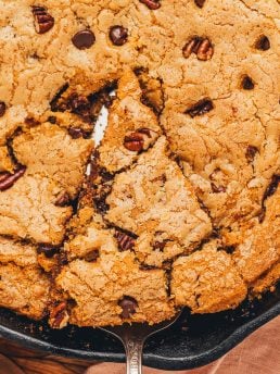 A slice of chocolate chip cookie being lifted out of the main dish.