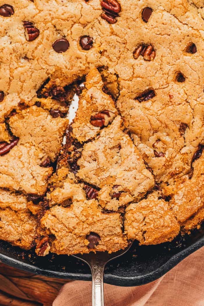 A slice of chocolate chip cookie being lifted out of the main dish.
