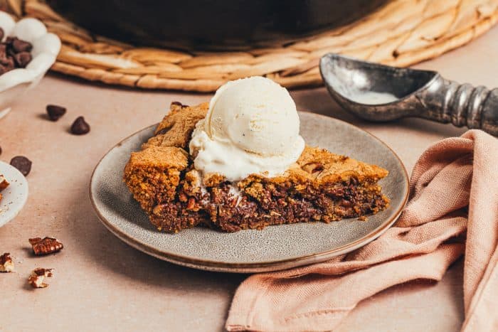 A plate with a slice of brown butter pecan chocolate chip skillet cookie and a scoop of ice cream.