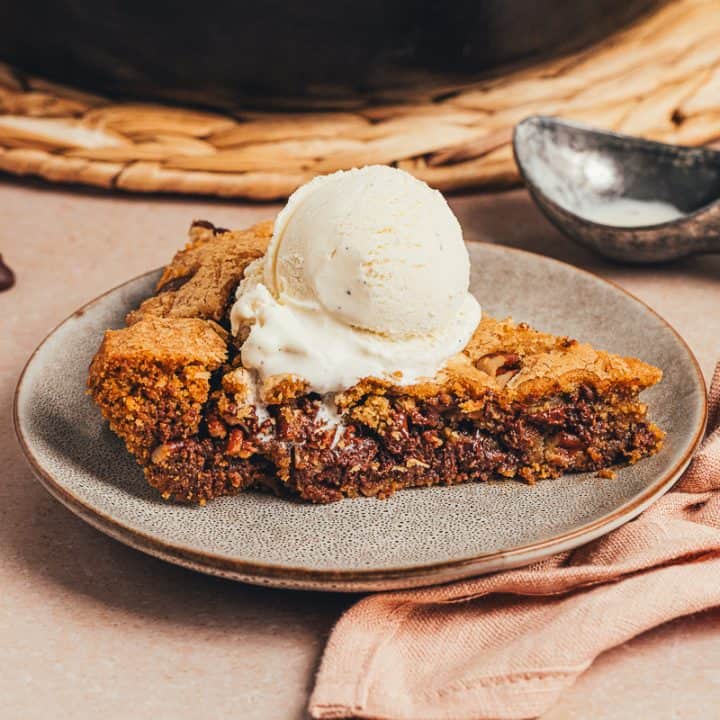 A plate with a slice of brown butter pecan chocolate chip skillet cookie and a scoop of ice cream.