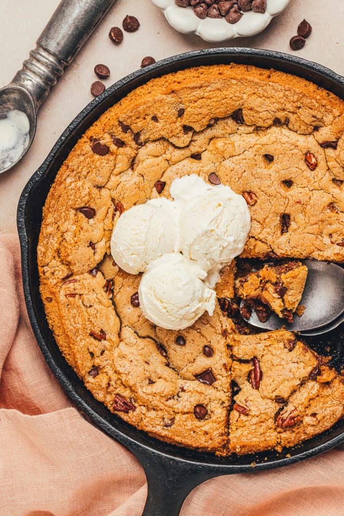 An image of the whole chocolate chip cookie skillet with two slices removed and a few scoops of ice cream in the middle.