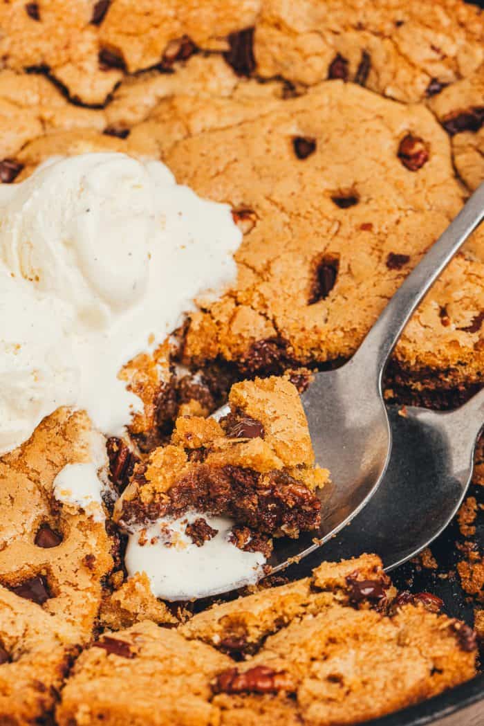 A spoon with a bite of chocolate chip cookie skillet and melted ice cream.