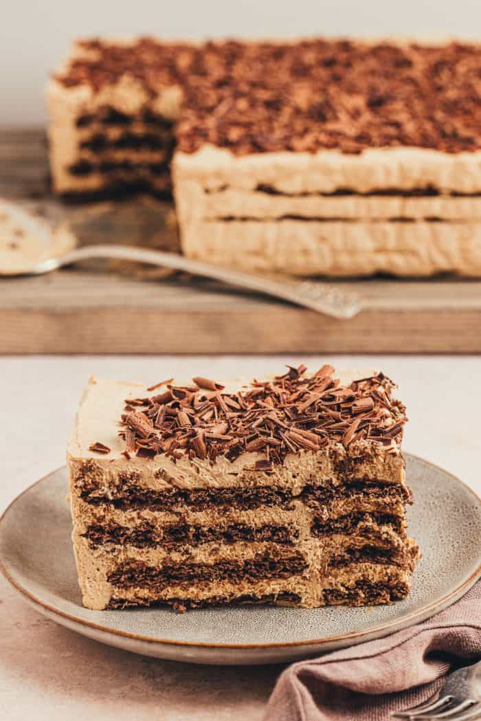 A slice of the homemade espresso icebox cake on a plate with the whole cake in the background.