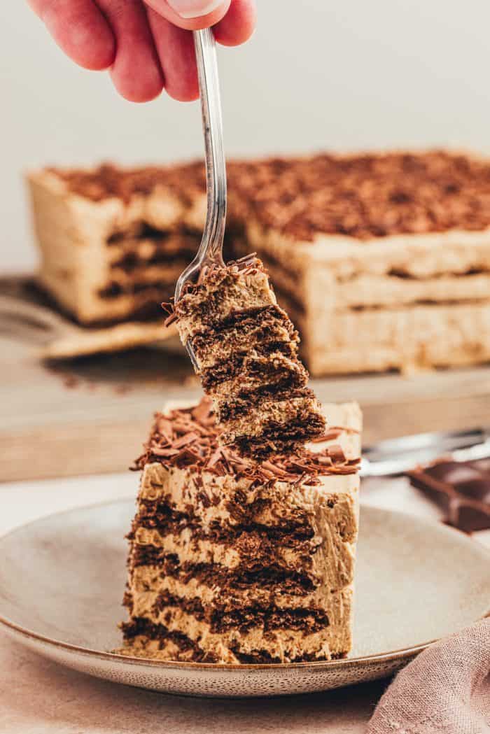 A slice of the homemade espresso icebox cake on a plate with the whole cake in the background.