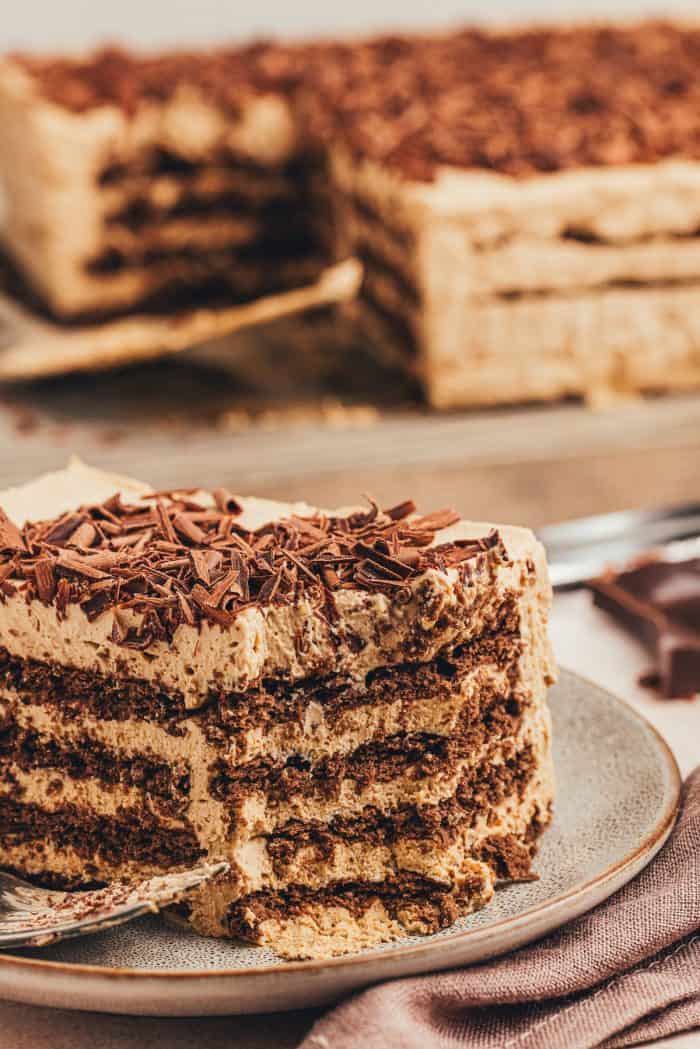 A slice of the homemade espresso icebox cake on a plate with the whole cake in the background.