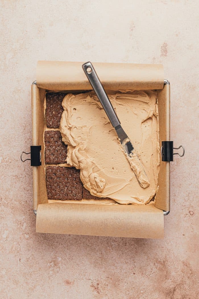 Graham crackers spread over espresso cream with more cream being spread over it in a square pan.