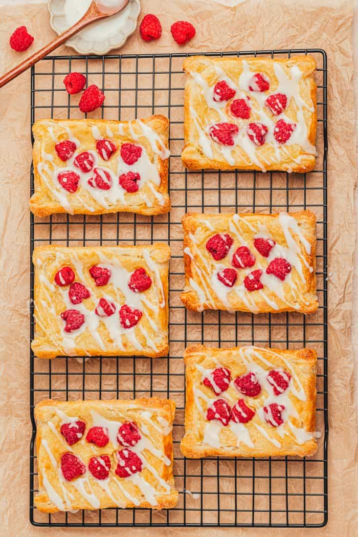 Freshly baked and iced raspberry cream cheese danishes on a cooling rack.