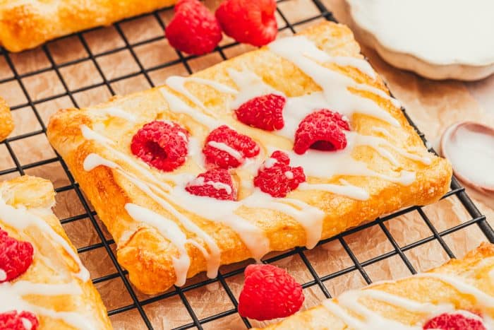 A few raspberry lemon cream cheese danishes on a cooling rack with fresh raspberries scattered around.