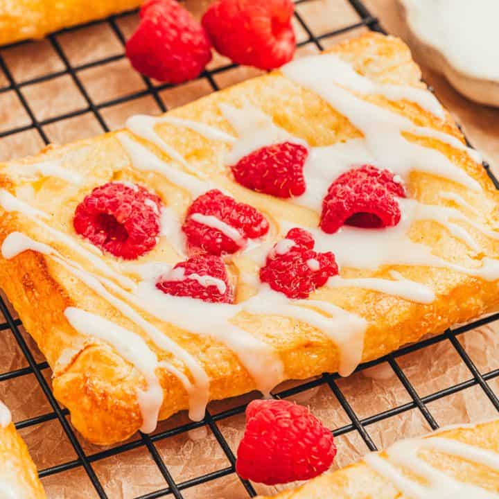 A few raspberry lemon cream cheese danishes on a cooling rack with fresh raspberries scattered around.