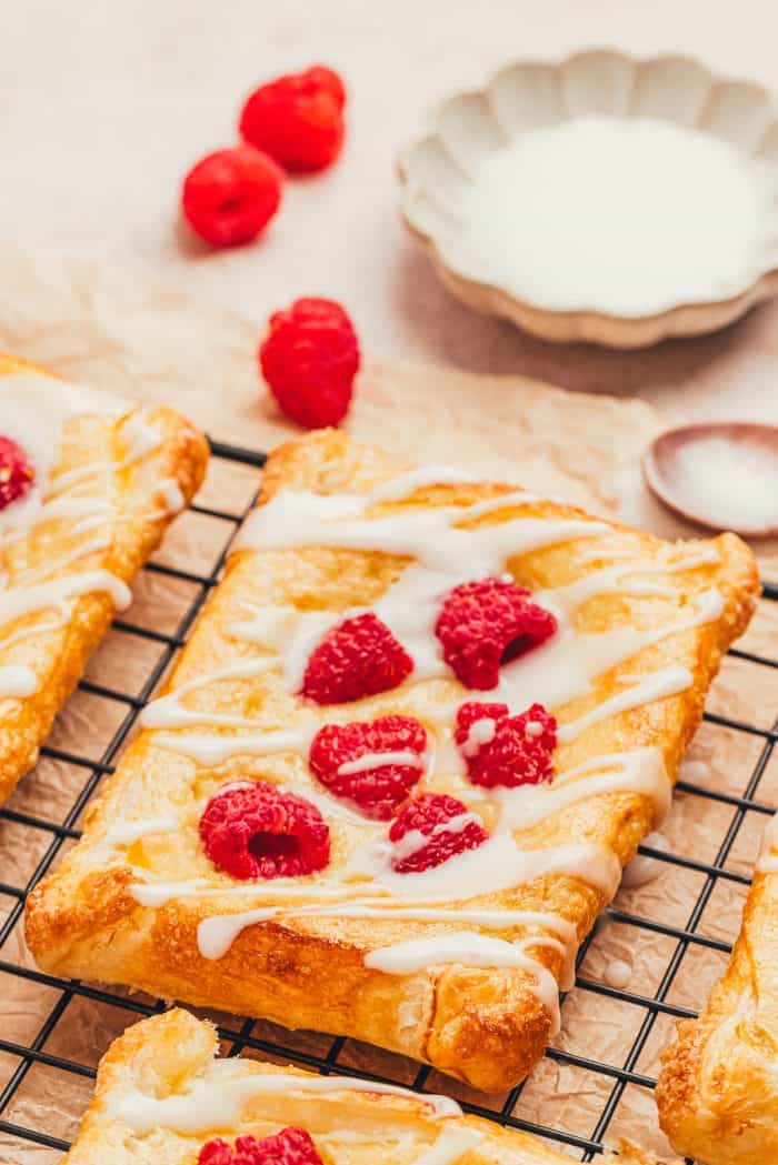 A few raspberry lemon cream cheese danishes on a cooling rack with fresh raspberries scattered around.