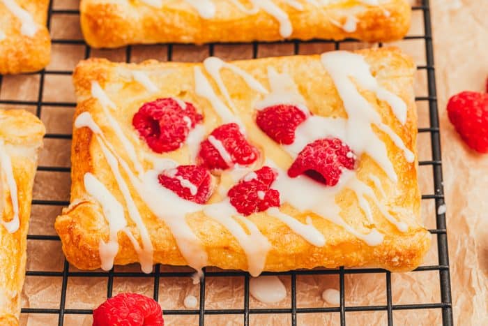 A few raspberry lemon cream cheese danishes on a cooling rack with fresh raspberries scattered around.