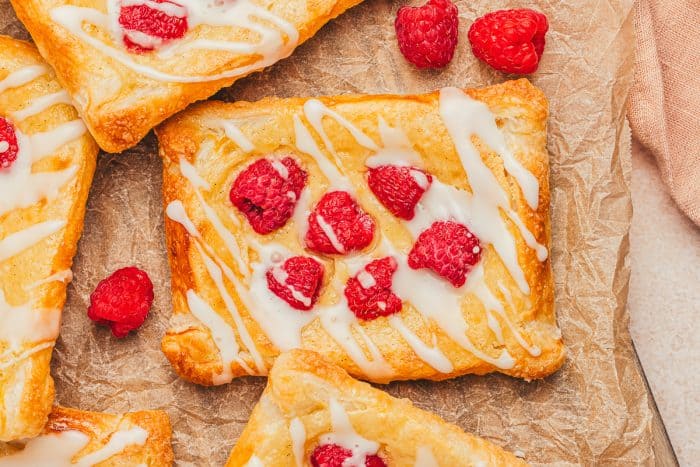 A few raspberry lemon cream cheese danishes on parchment paper with fresh raspberries scattered around.