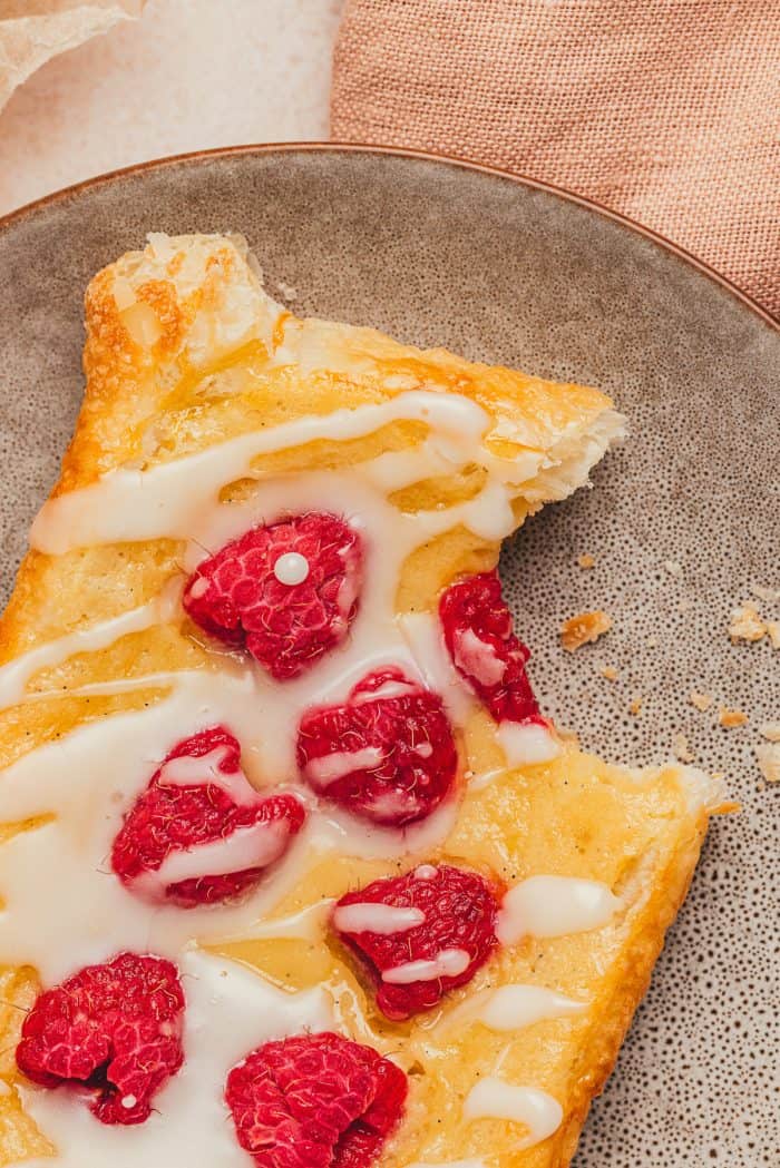 A homemade raspberry danish with a bite taken out of it on a plate.