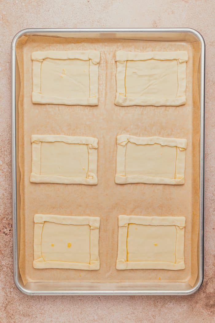 Raw puff pastry with the edges folded over on a baking sheet.