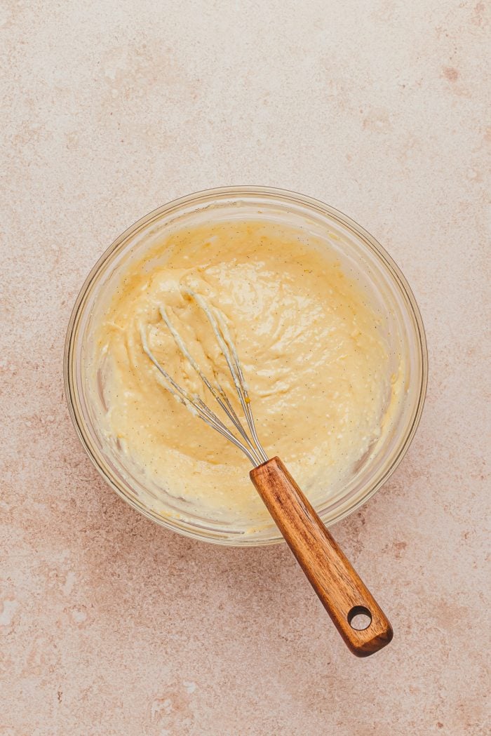 A glass bowl with the cream cheese danish filling being stirred with a whisk.