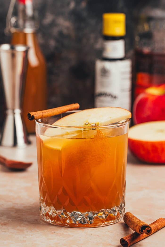 A glass of Apple Cider Old Fashioned with bottles behind.