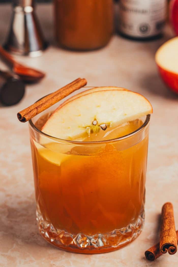 A glass with an Apple Cider Old Fashioned and garnished with an Apple slice and a cinnamon stick.