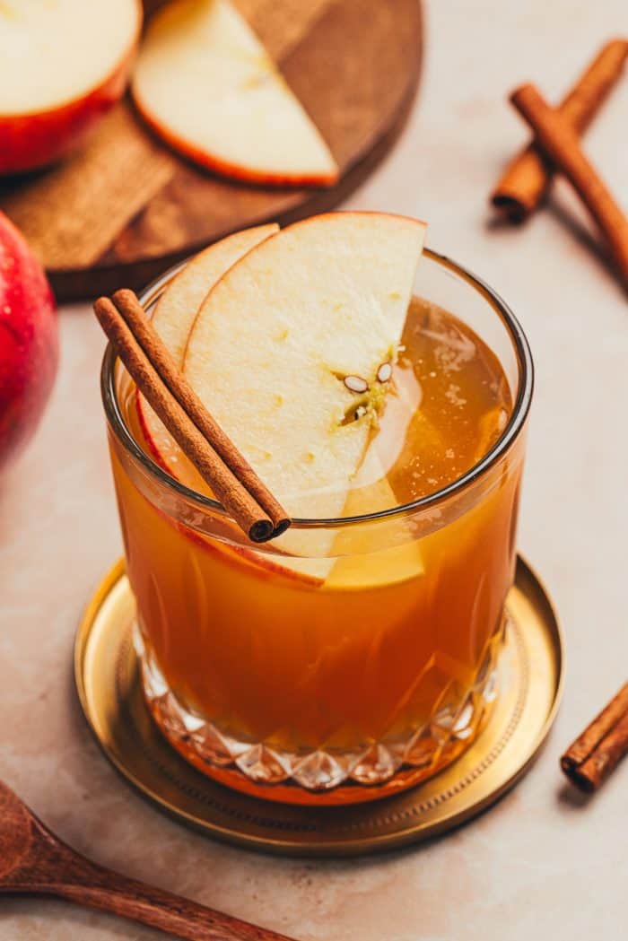 A glass with an Apple Cider Old Fashioned and garnished with two apple slices and a cinnamon stick.