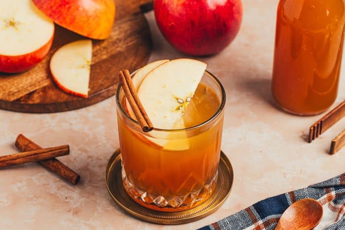 A glass of Apple Cider Old Fashioned with cinnamon sticks and apple slices.