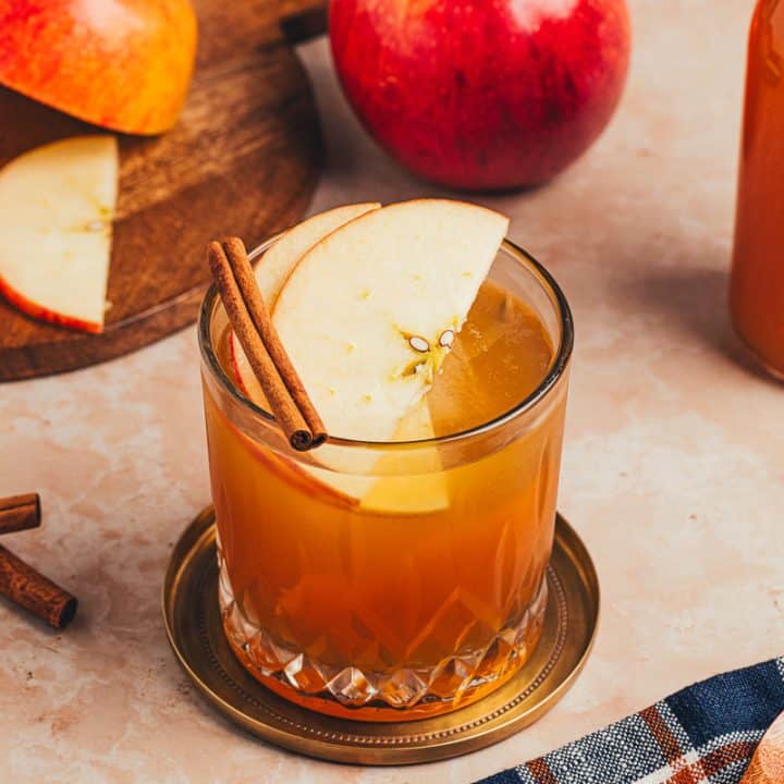 A glass of Apple Cider Old Fashioned with cinnamon sticks and apple slices.