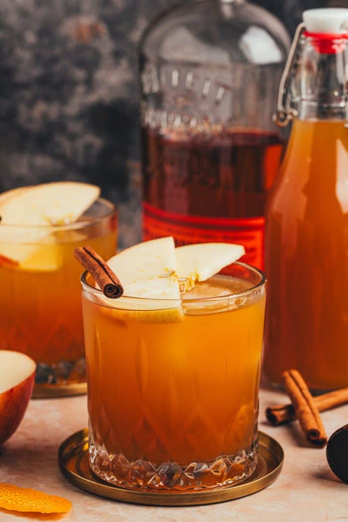 A glass with an Apple Cider Old Fashioned and garnished with two apple slices and a cinnamon stick.