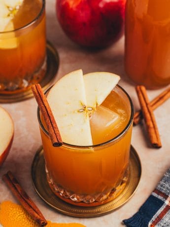 A glass with an Apple Cider Old Fashioned and garnished with two apple slices and a cinnamon stick.