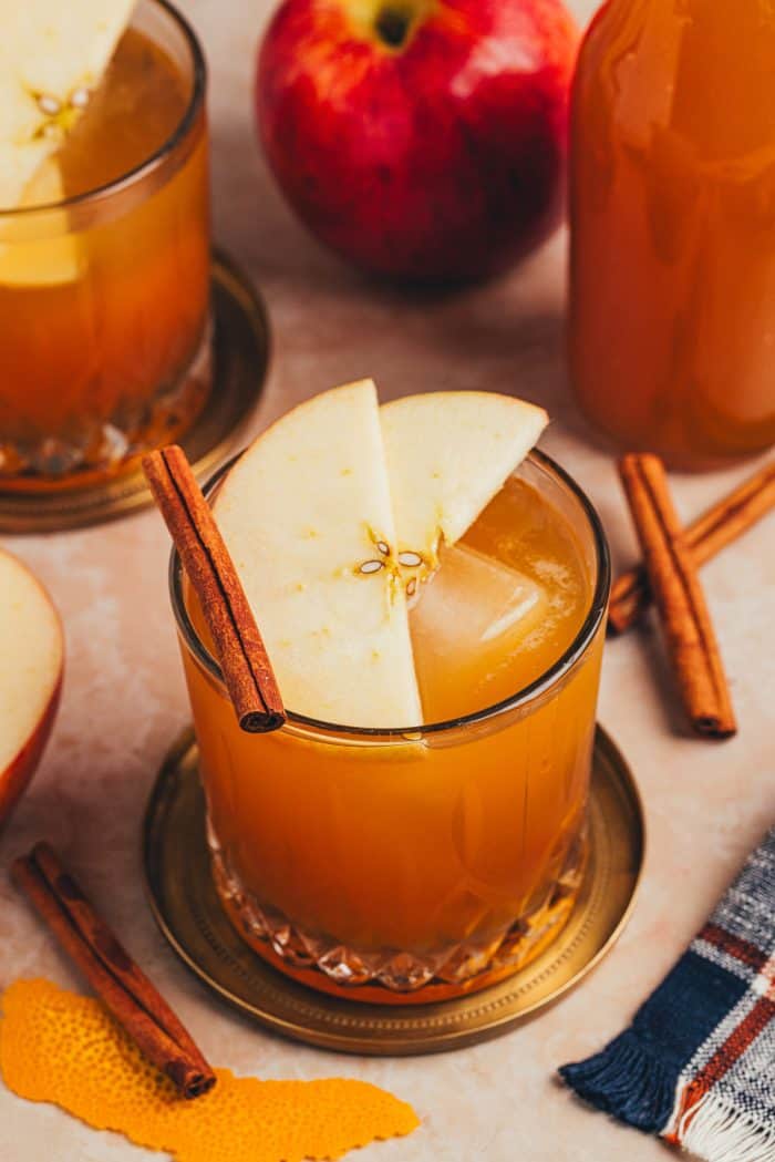 A glass with an Apple Cider Old Fashioned and garnished with two apple slices and a cinnamon stick.