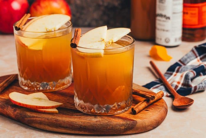 Two glasses of Apple Cider Old Fashioned with cinnamon sticks and apple slices.