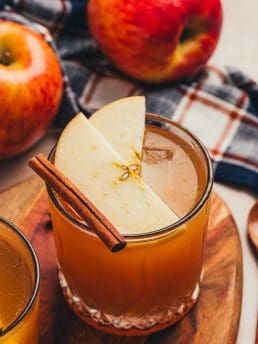 A glass with an Apple Cider Old Fashioned and garnished with two apple slices and a cinnamon stick.