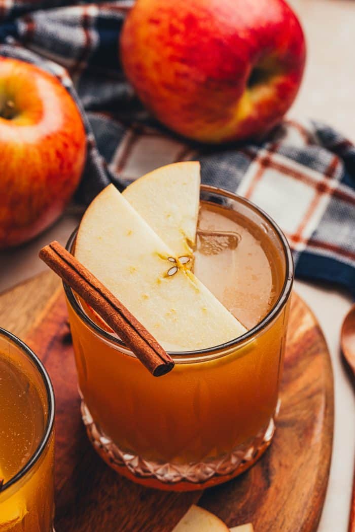 A glass with an Apple Cider Old Fashioned and garnished with two apple slices and a cinnamon stick.