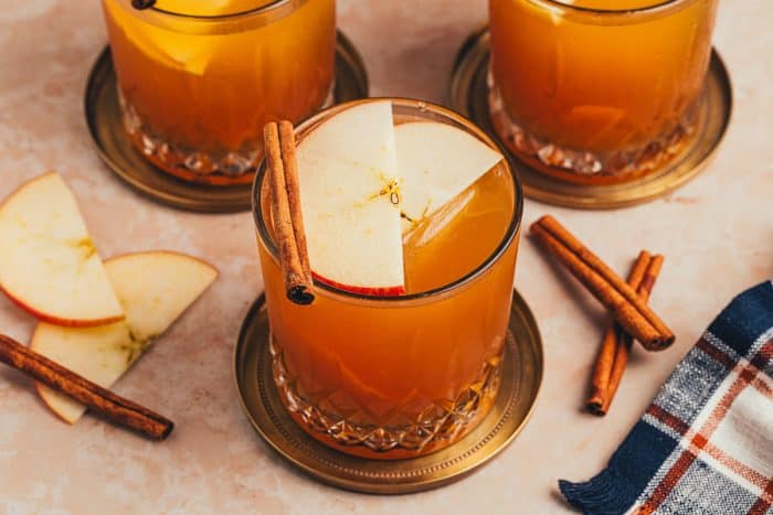 Three glasses of Apple Cider Old Fashioned with cinnamon sticks and apple slices.