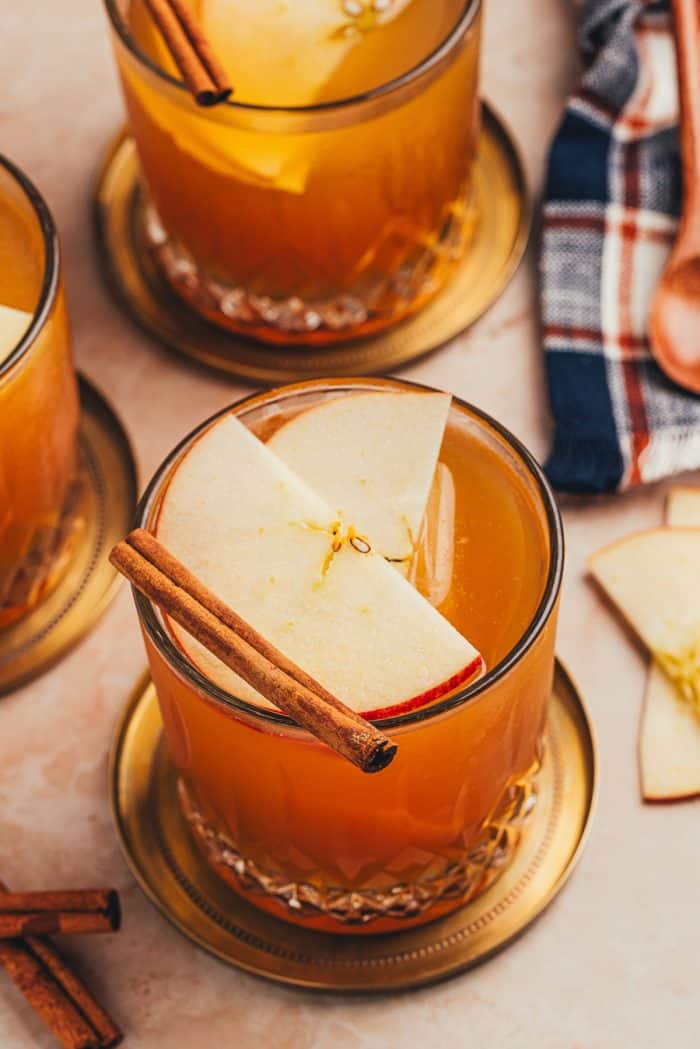 A glass with an Apple Cider Old Fashioned and garnished with two apple slices and a cinnamon stick.