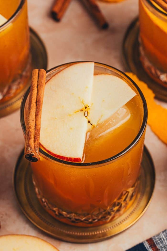 A glass with an Apple Cider Old Fashioned and garnished with two apple slices and a cinnamon stick.