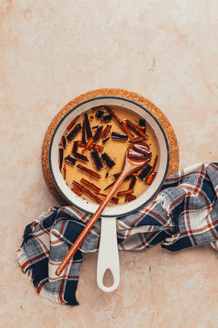 A saucepan with cinnamon syrup in it and a wooden spoon.