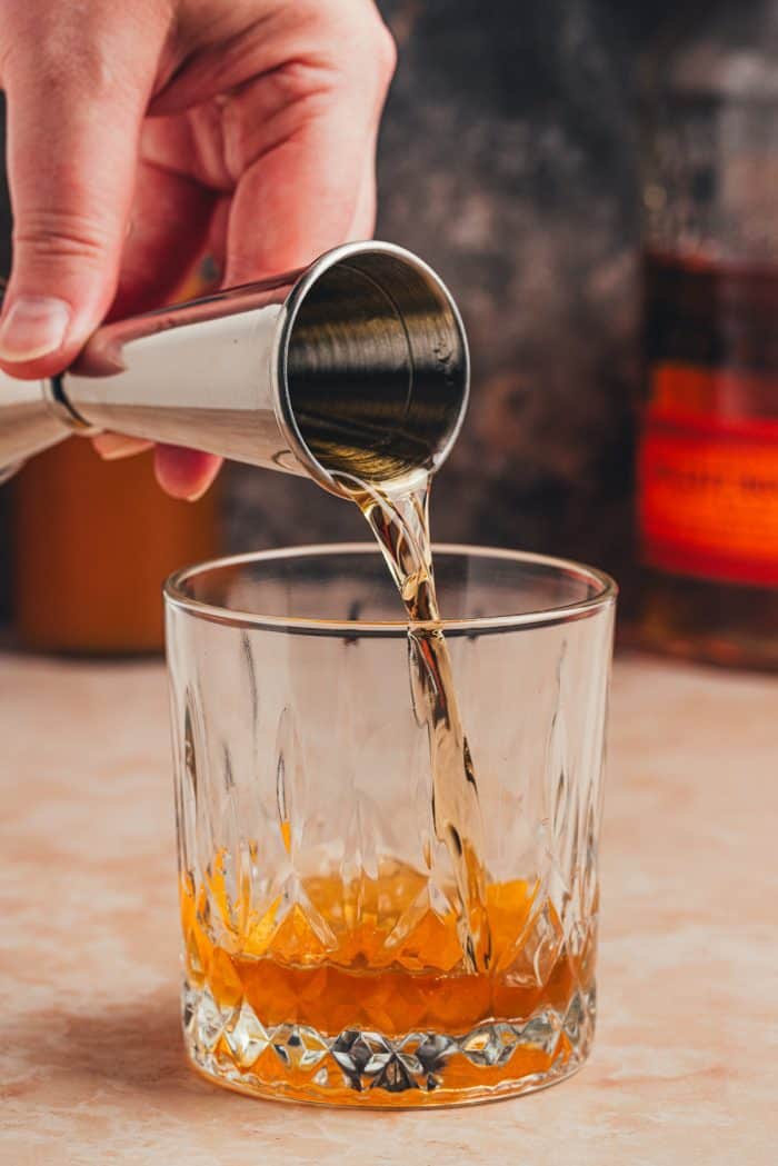 Alcohol being poured into a glass with an orange peel.