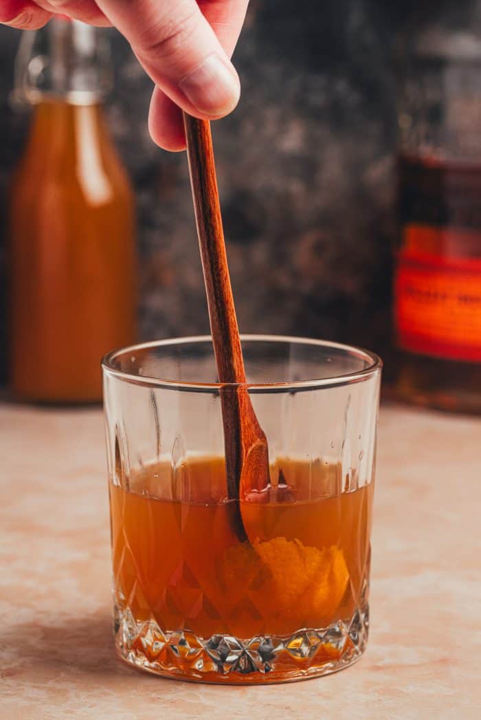 A wooden stick stirring the Apple Cider Old Fashioned.