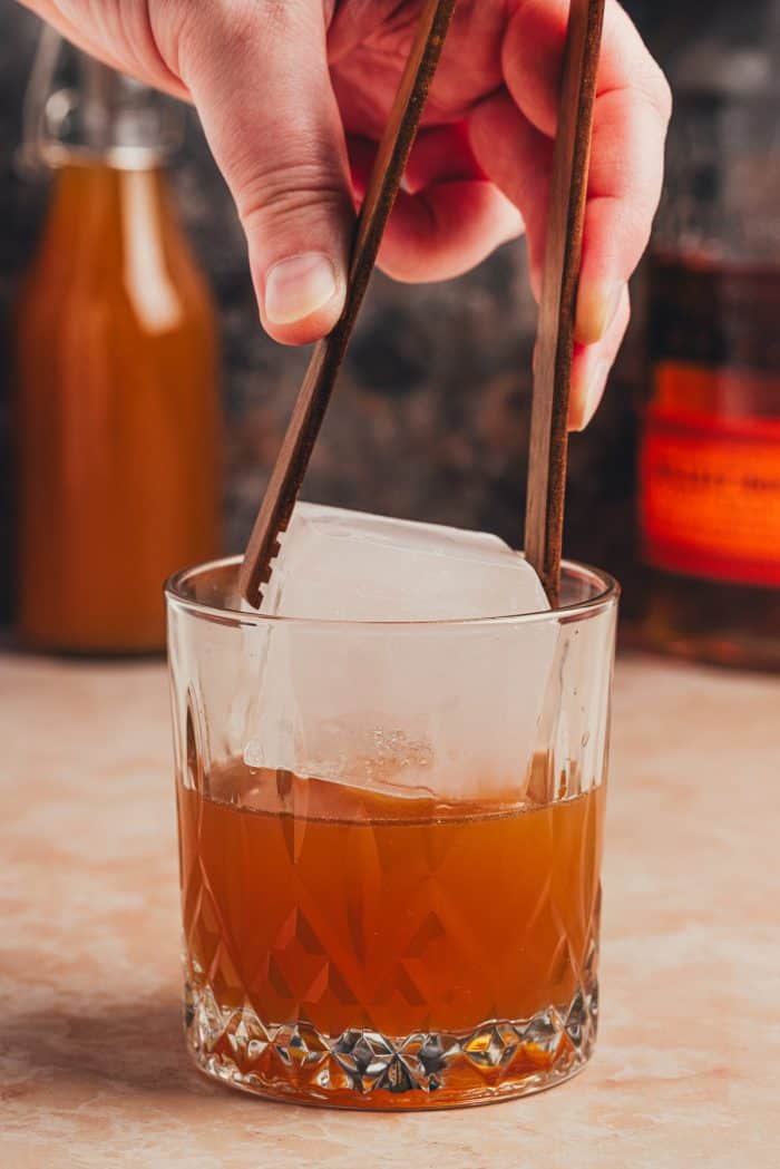 A large ice cube being placed into a glass.