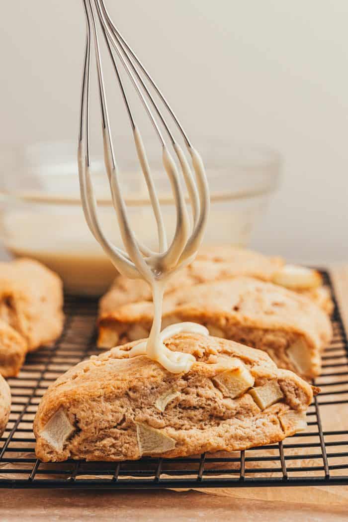 Apple cinnamon scones being drizzled with a maple glaze on a black wire rack.