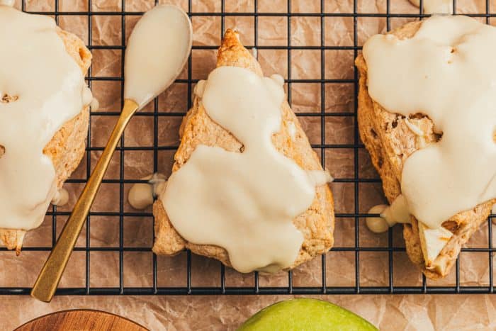 Apple cinnamon scones on a wire rack with a spoon with maple glaze.